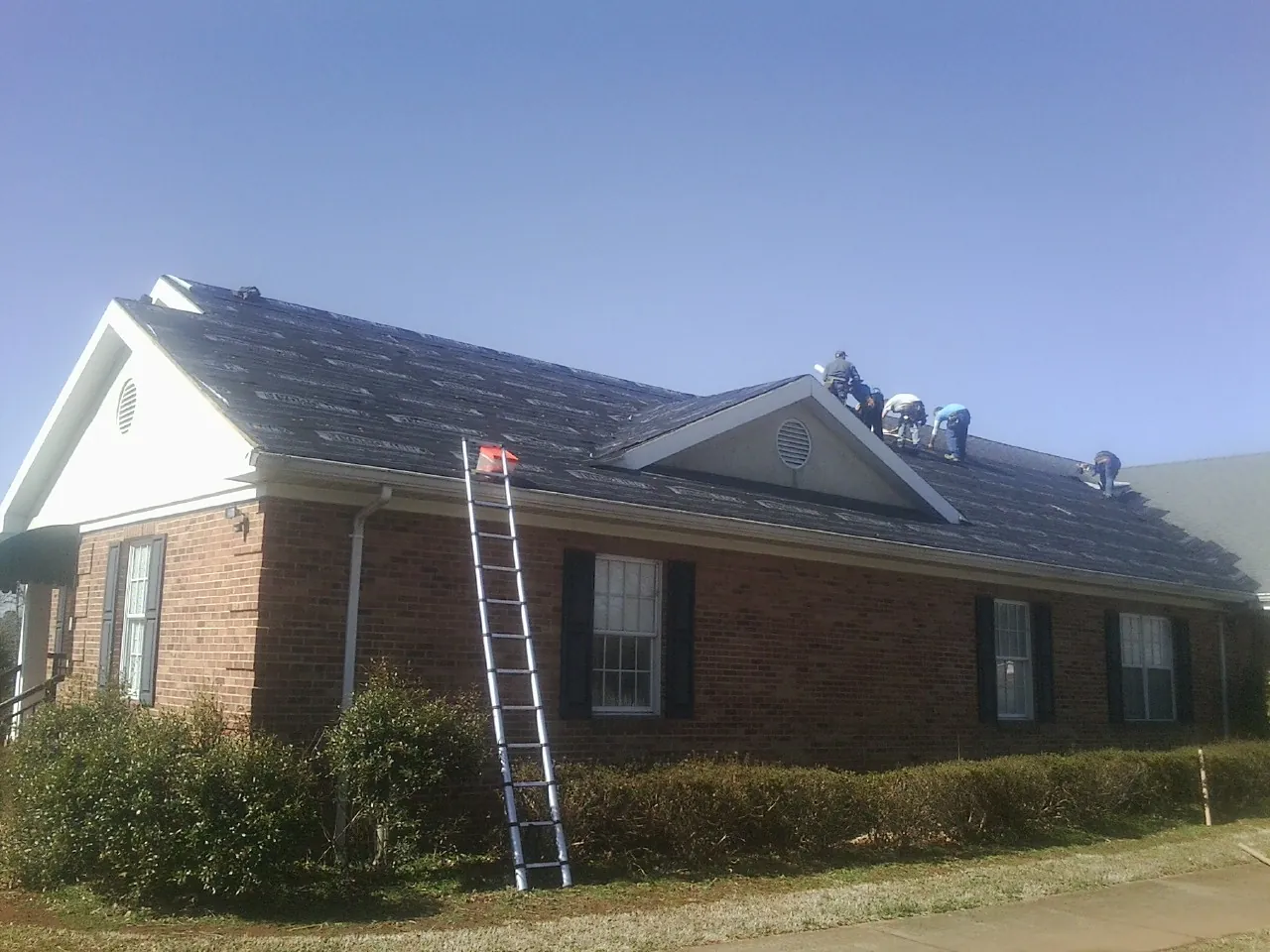 Crew tearing shingles off a brick ranch roof with a ladder set — Metal Roof Repair work by our crew in Berlin Center