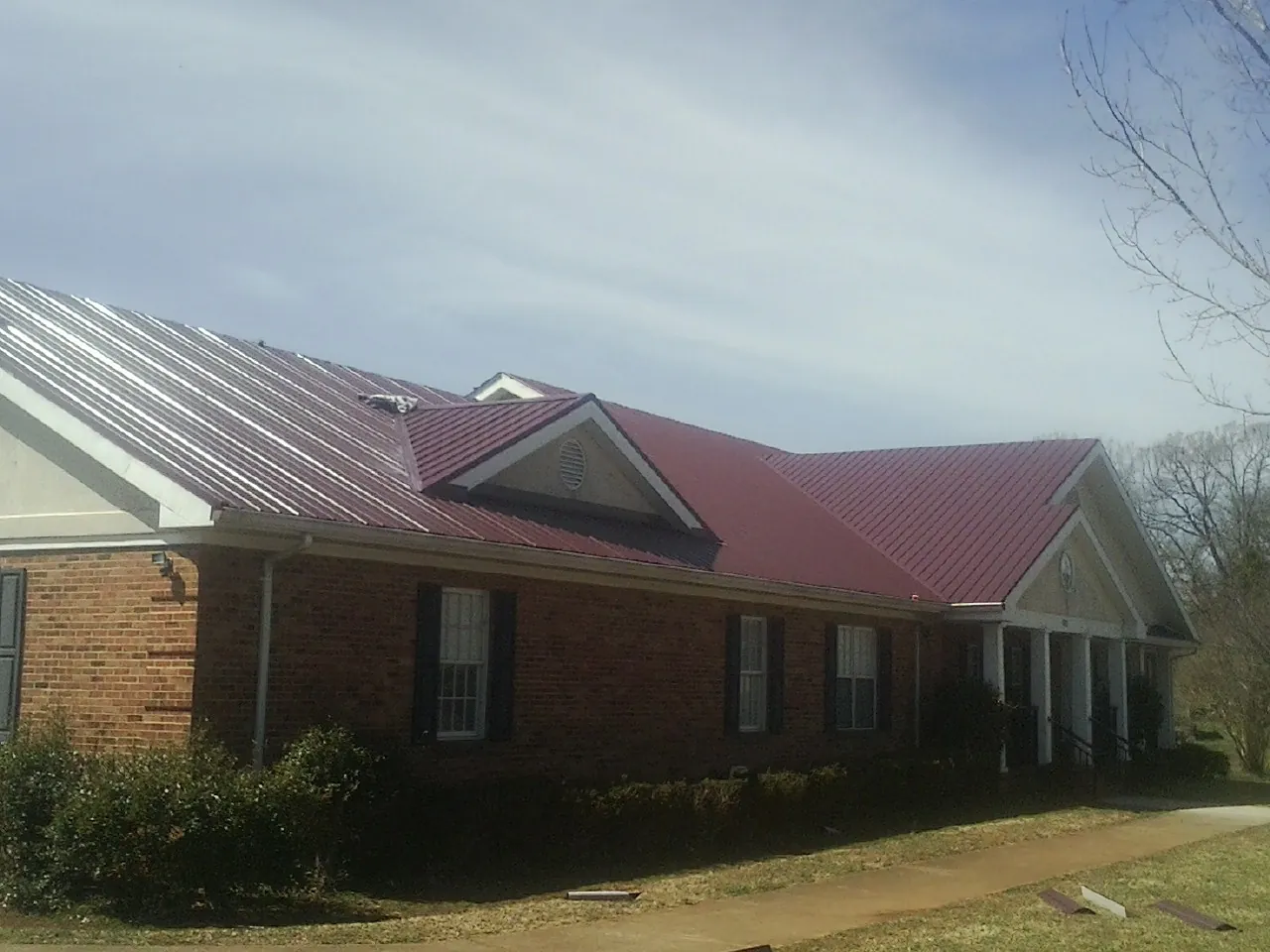Red metal roof with gabled entries on a long brick building, from a Hail Damage Roof Repair job in Berlin Center