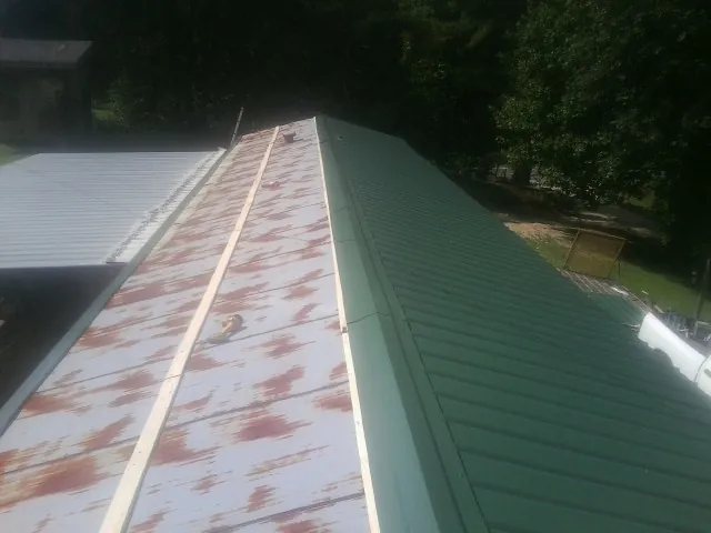 Old rusted panels beside newly installed green metal roofing — Wind Damage Roof Repair by Roofing Brothers in Berlin Center
