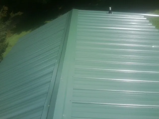 New green metal panels meeting at the ridge of a roof — Flat Roof Repair work by our crew in Berlin Center