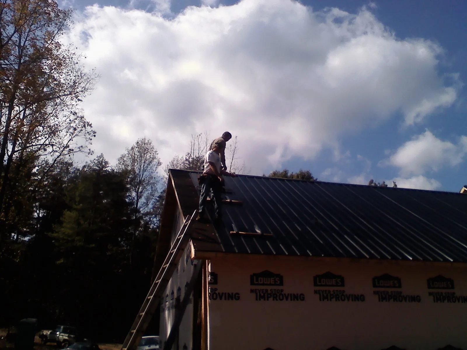 Roofer fastening dark metal panels high against a cloudy sky, from a Roof Inspection job in Berlin Center