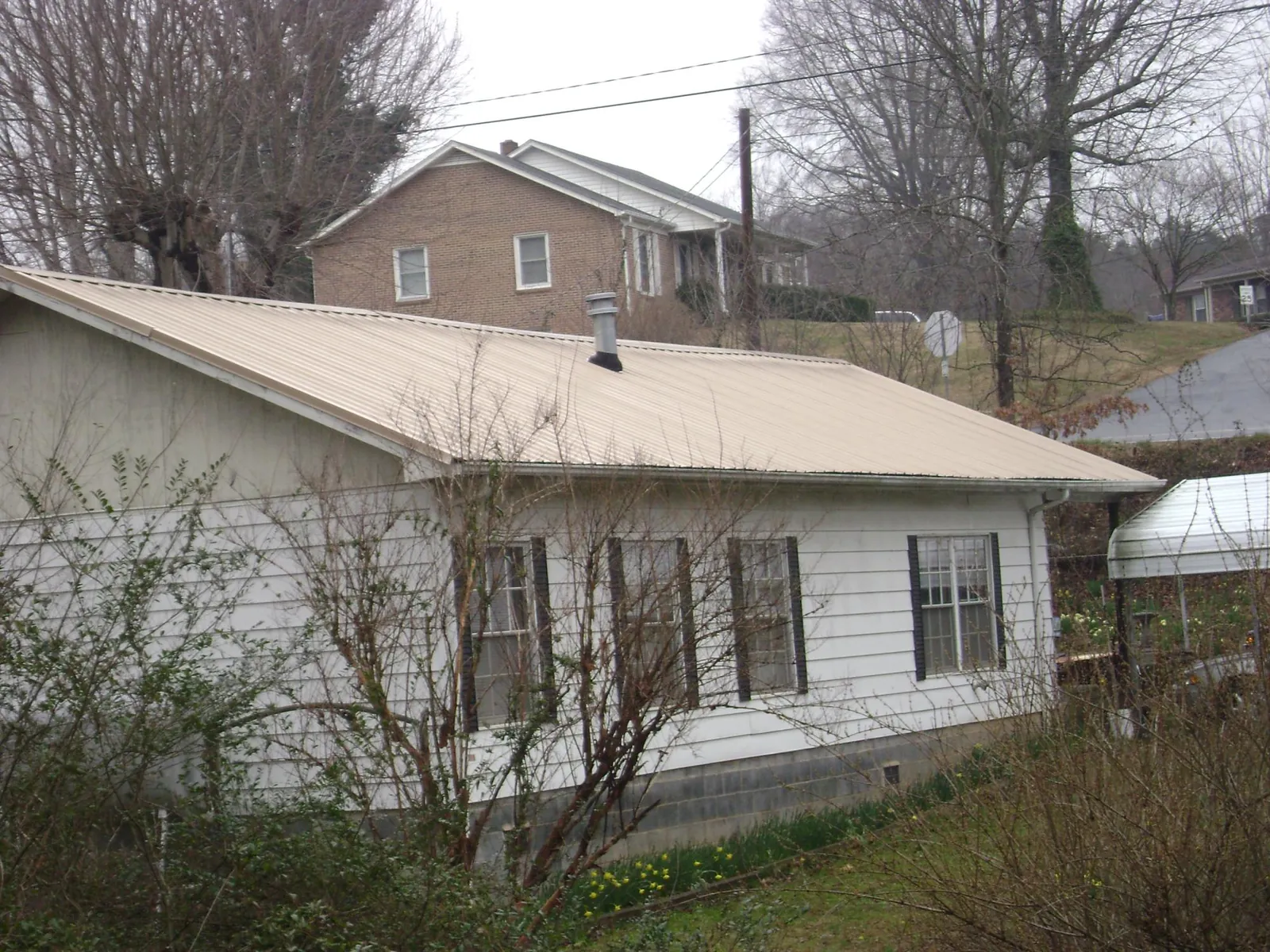 Tan metal roof on a white sided house set into a hillside — Commercial Roofing by Roofing Brothers in Berlin Center