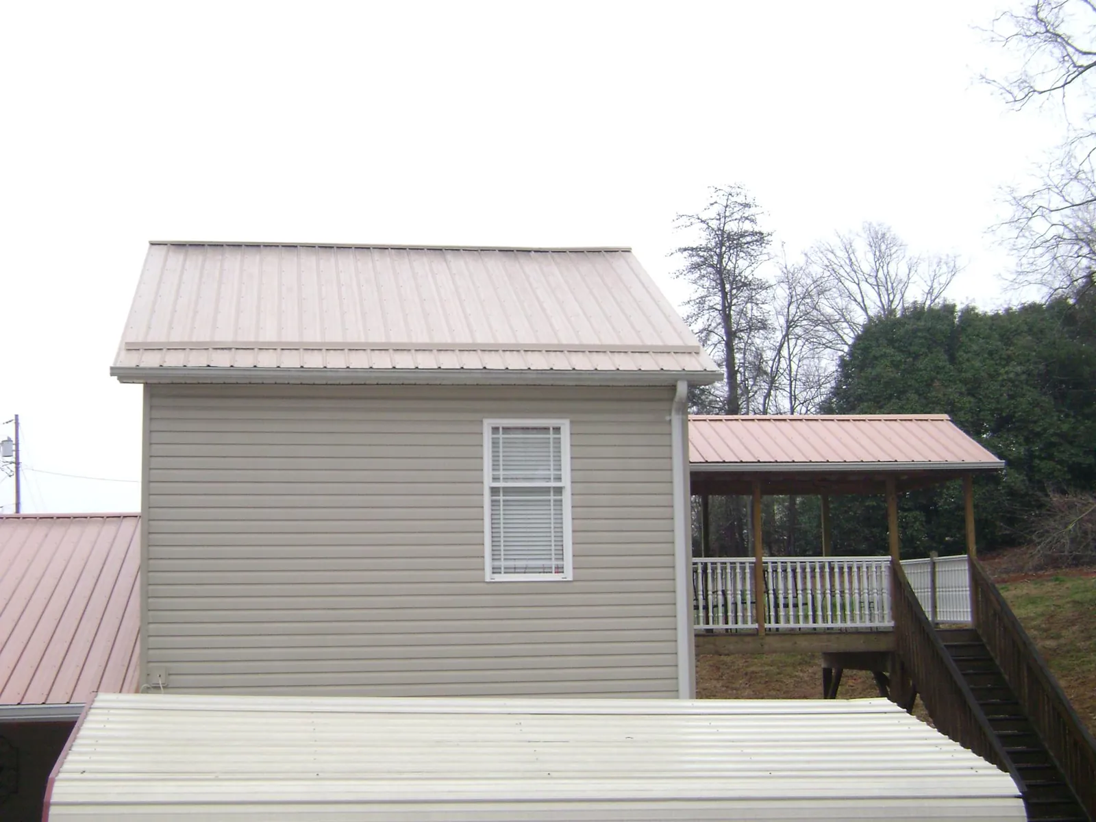 Tan metal roofs on a two story addition and attached porch, from a Roof Replacement job in Berlin Center